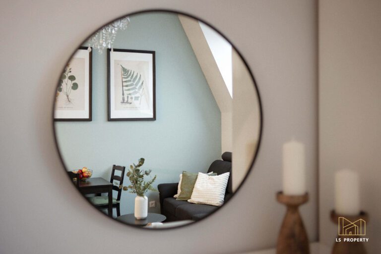 Okrągłe lustro w cienkiej czarnej ramie wiszące na ścianie.